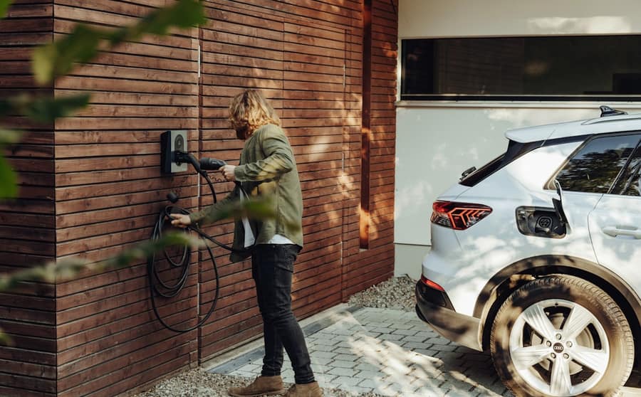 A car being plugged into a wall-mounted charger beside a house